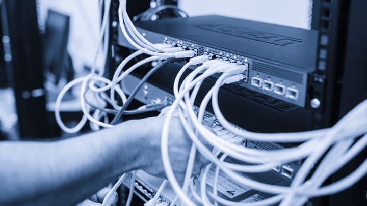 Mãos de um técnico conectando cabos de rede em equipamentos montados em rack