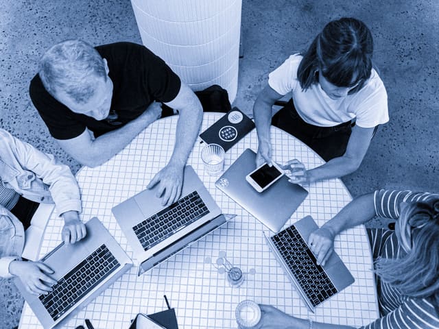 Pessoas trabalhando lado a lado com notebooks sobre uma mesa
